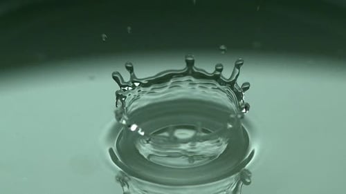 Wassertropfen, der vor grünem Hintergrund ins Wasser fällt, Zeitlupe