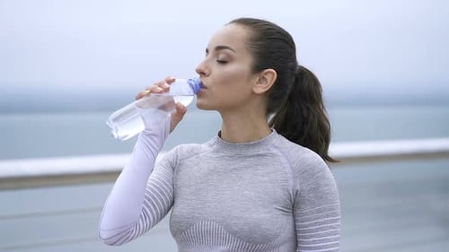Brunette Woman Drinks Water After Exercise by Ocean
