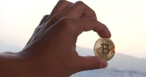 Hand Holding Bitcoin Against Sunrise