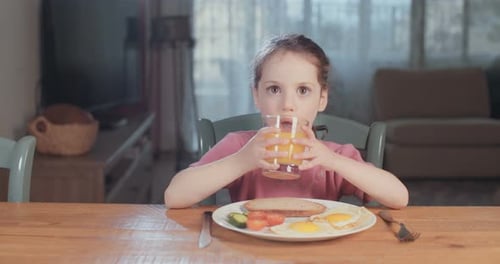 Young Girl Drinks Orange Juice at Breakfast Table