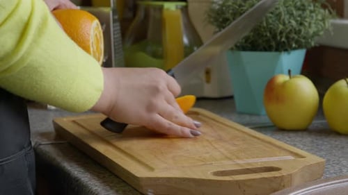 Housewife Slices Orange with Knife on Wooden Board. Hands Close-up.