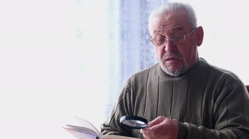 Senior Man Reads Book with Magnifying Glass