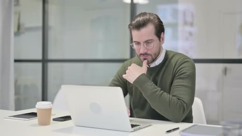 Junger Geschäftsmann denkt bei der Arbeit am Laptop im Büro