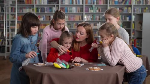 Girls Decorating Cookies With Teacher in School Library