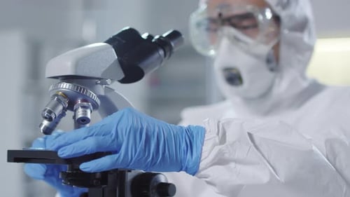 Scientist in Protective Gear Using Microscope