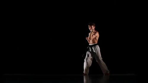 Homme s'entraînant au taekwondo ou au karaté, au saut, au coup de pied haut et au poing isolé sur fond noir