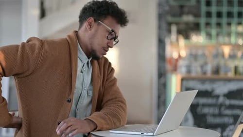 African Man Having Back Pain While Using Laptop in Cafe