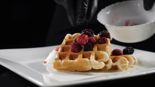 Hands placing raspberries on waffles with berries