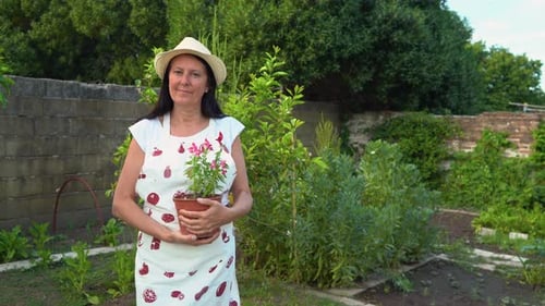 Middle-aged woman smiling in her home garden and holding a pot of flowers