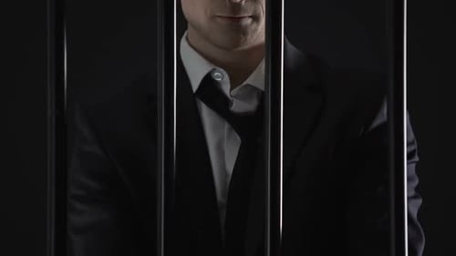 Man Holding Money Behind Prison Bars in Handcuffs