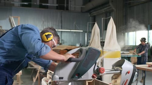 Man Cutting Wood with Miter Saw in Workshop