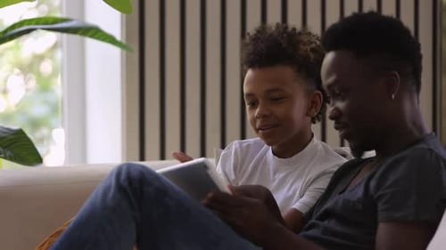 Hombre afroamericano hablando y usando una tableta en el sofá de la habitación de casa Spbi
