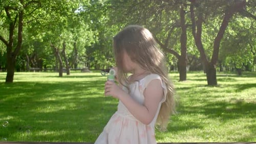 Girl Blowing Bubbles in a Sunny Green Park