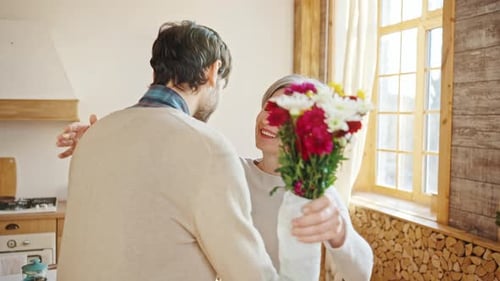 Man Gives Flowers to Happy Senior Woman Indoors