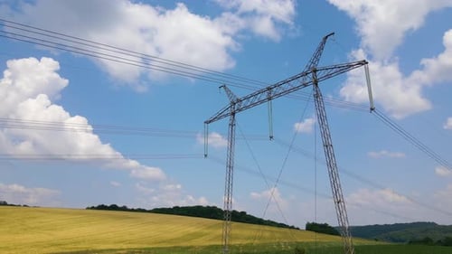 High Voltage Tower with Electric Power Lines Between Green Agricultural Fields
