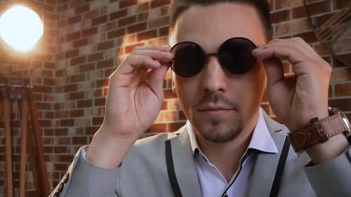 Man Puts on Round Sunglasses in Studio Setting