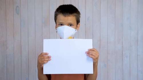 Little Latin Boy in a Medical Mask Looking at the Camera Holding a Sheet of A4 Paper. Mockup in the