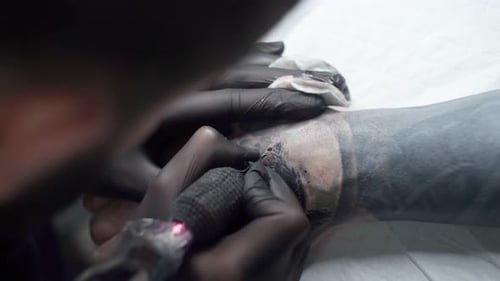 Tattoo-Meister, der Tätowierung mit Maschine auf dem Arm im Salon malt