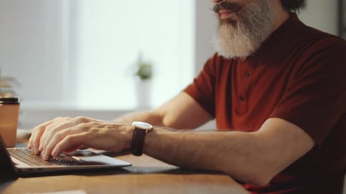 Close Up of Bearded Businessman Typing on Laptop at Office Desk