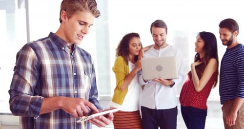 Executive using digital tablet while colleague discussing in background
