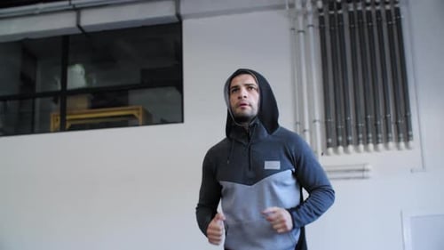 A Man in a Gray Jacket with a Hood Runs in the Gym