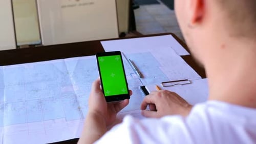 Construction engineer using a smartphone with a green screen looking for information on the internet