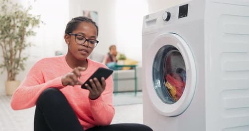 Woman Using Phone While Doing Laundry at Home