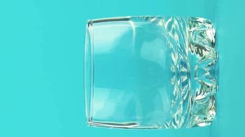 Pouring yellow liquid into clear glass on blue
