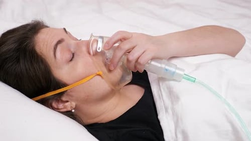 Une jeune femme masquée s'allonge sur le lit et commence à tousser et à haleter