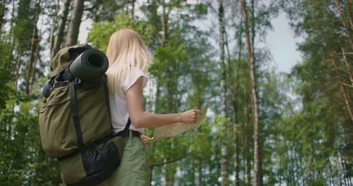 Slow Motion of a Young Tourist Woman with a Road Card and a Compass in the Woods, Searching for the