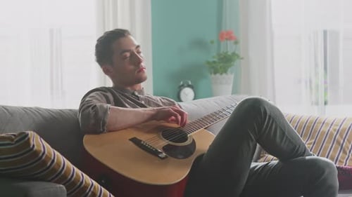 Man Playing Acoustic Guitar While Relaxing on Couch