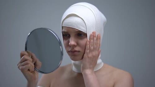 Woman with Bandage Holds Mirror in Hospital Setting