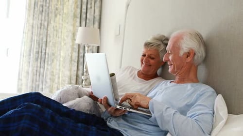 Senior Couple Relaxing in Bed with Laptop