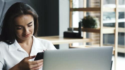 Happy and Charming Freelance Woman Using Her Phone and Having Laptop in Cafe