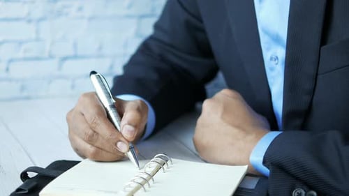 Man Hand Writing on Notepad While Sited