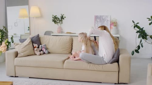 Woman Brushing Child's Hair on Couch at Home
