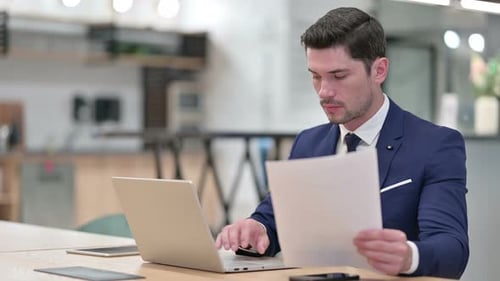 Businessman Working on Laptop with Documents in Office