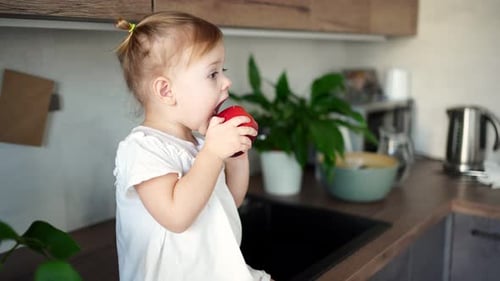 Happy Child Eating a Red Apple in Kitchen
