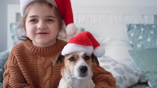 Child Cuddles Dog Wearing Santa Hat Indoors