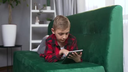Small Boy which Lying on Green Sofa at Home and Using Tablet PC