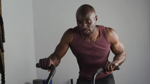 Fit african american man exercising on training bike inside gym