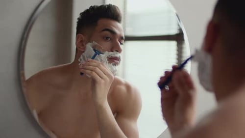 Handsome Young Adult Shaving in Bathroom Mirror