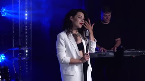 A Stylish Girl Vocalist Sings on Stage in a Vintage Microphone. In the Background a Man Playing