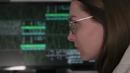 Hacker tries to hack into the system. A female hacker works at a computer at night in the dark.