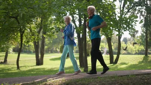 Side View Happy Senior Couple Running in Slow Motion in Sunrays Outdoors Smiling