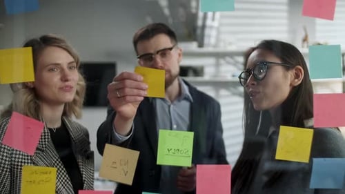 Team Brainstorming Together on Glass Wall in Office