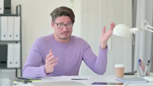Frustrated Man Gestures at Desk in Bright Office