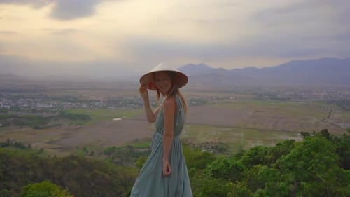 A Young Woman Tourist Stands on a Mountain Top with an Amazing View on a Valley. She Wears an Asian