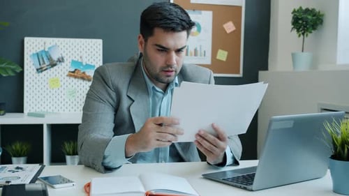 Empresario serio que trabaja con papeles mirando documentos y escribiendo sentado en el escritorio de la oficina