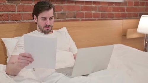 Young Adult Works from Bed with Laptop